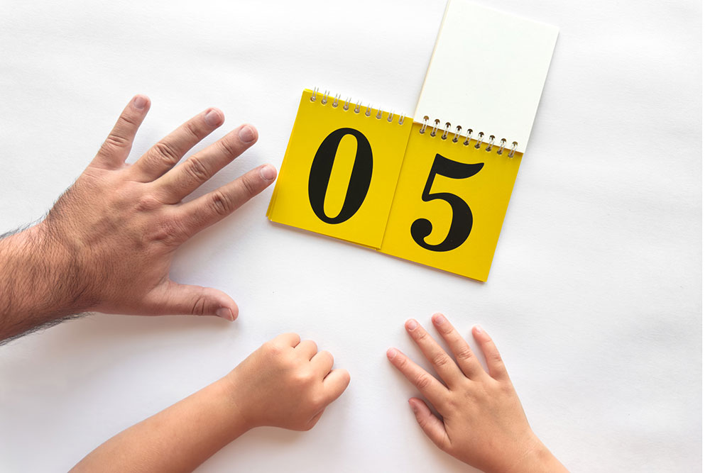Adult and child hands holding up fingers next to a calendar